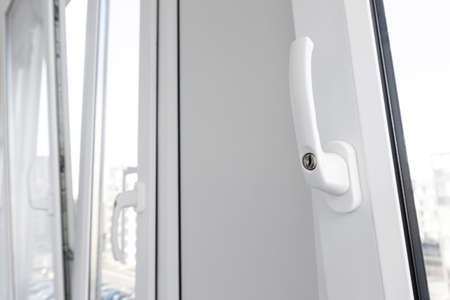 Opened white plastic window handle in upright position close-up. New tilt and turn pvc windows ventilation.の写真素材