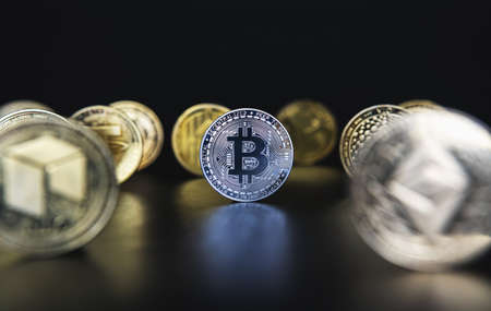 Silver Bitcoin next to many cryptocurrency coins like defocused Ethereum, Neo, Tether on black background. Central composition, low key photo for banners and news about BTC crypto.の写真素材
