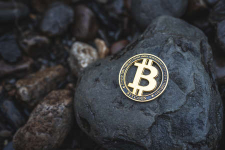 Bitcoin crypto coin with copy space for text. Close-up of single gold Btc cryptocurrency on rocks outdoor. Low key toned photo for banners and news.の写真素材