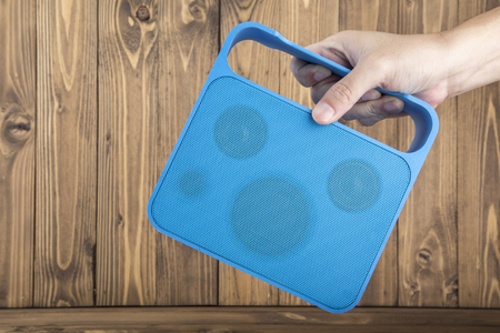 Man's Hand Carrying Blue Handy Speaker on Wooden Background