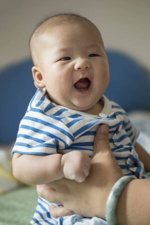 Mother's hands Holding Happy Smiling Asian Baby Boy in Blue and White Striped Shirtの写真素材