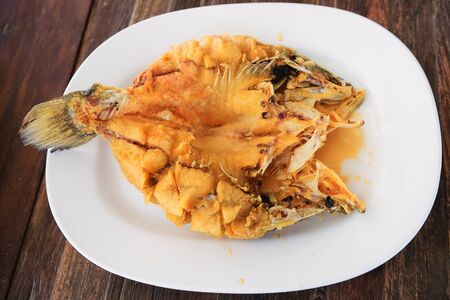 Deep-fried marinated snapper with sweet fish sauce served on white plate on wooden table.