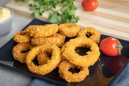 Fried onion rings on a black plate with tomato and parsleyの写真素材