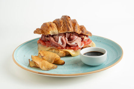 Croissant sandwich with bacon and potato chips on a blue plateの写真素材