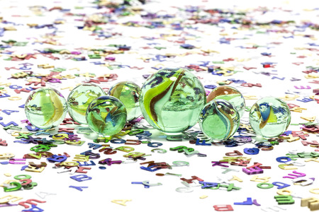 Toy marbles on white background, surrounded by so many multicolor letters の写真素材