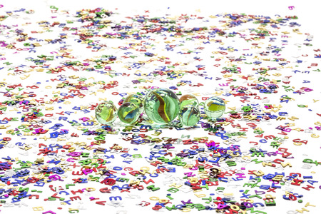 Toy marbles on white background, surrounded by so many multicolor letters の写真素材
