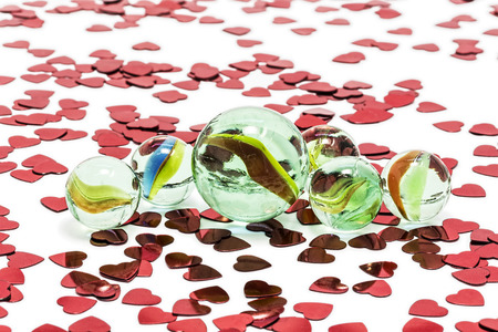 Toy marbles on white background, surrounded by so many red hearts の写真素材