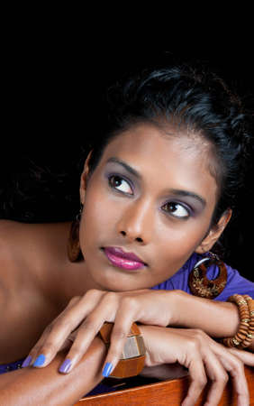 beautiful woman of east indian ancestry looking away from you with chin resting on chair arm の写真素材