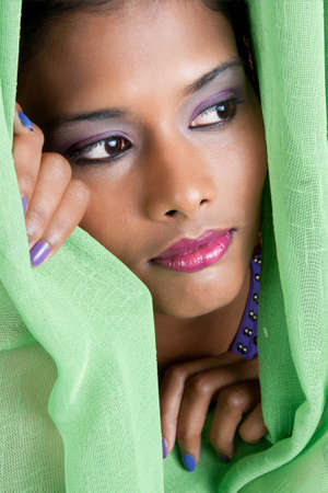 beautiful woman of east indian descent looks from behind a green curtain の写真素材