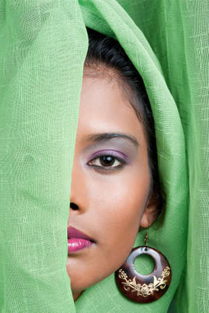 beautiful woman of east indian descent looks from behind a green curtain の写真素材