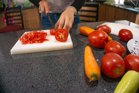 woman cutting vegetables tomato and carrots on cutting board in the kitchen with knifeの写真素材