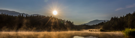 Panoramic view of a foggy lake in the mountains at sunriseの写真素材