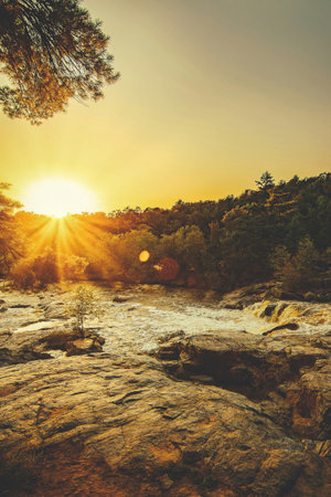Beautiful sunset over a mountain river with rocks and trees in the foregroundの写真素材