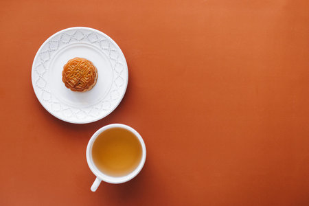 Mooncake and cup of tea on orange background. Top view.