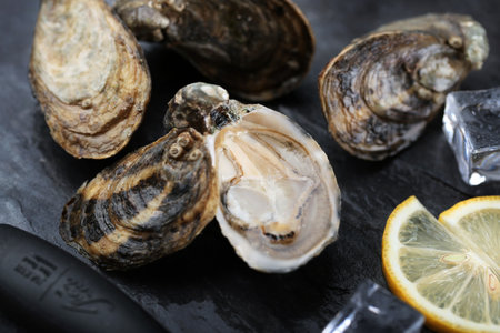 Fresh oysters with ice and lemon on black background, closeup