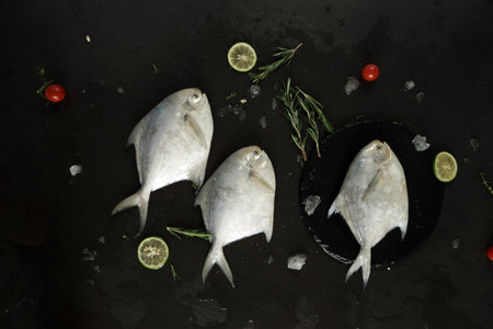 Fresh fish on a black background with rosemary, lime and tomatoesの写真素材