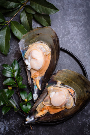 Fresh raw mussel on black plate with green leaves, top view