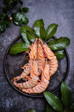 Raw tiger prawns on black plate with green leaves. Top viewの写真素材