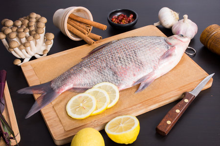Fresh fish on a cutting board with lemon, garlic, pepper and spices