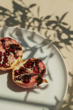 Pomegranate fruit with seeds on a white plate with shadowの写真素材
