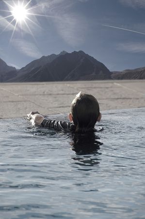Boy about 8 years old, inside the swimming pool and watching a bright sun in the sky, as the rays of light align with the smoke coming out of an airplane.の写真素材