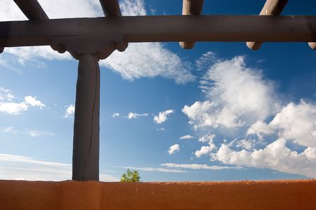 Southwestern architecture. Beams and earth colored wall against blue sky, one little tree showing up behind the wall. New Mexico の写真素材