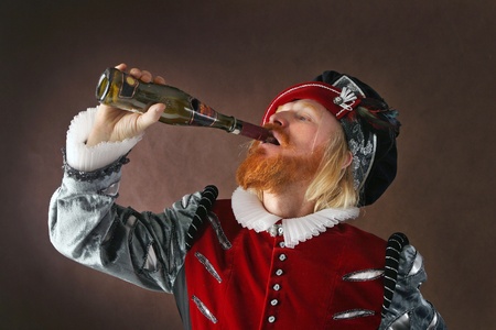 close-up portrait of a man of the Middle Ages with a beard and mustache in a suit isolated on a dark background drinking from a bottleの写真素材