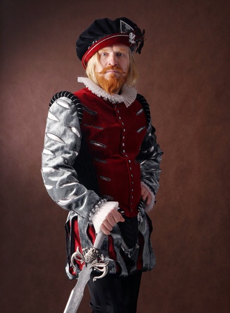close-up portrait of a man of the Middle Ages with a beard and mustache in a suit isolated on a dark background with a sword standingの写真素材