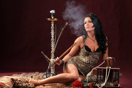 portrait of a girl sitting on a fur skin smokes hookah studioの写真素材
