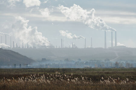 Man-made landscape of dry grass in the field and industrial part of the city and smoking chimneys on...