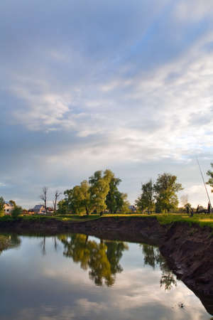 summer landscape oak grove on the shore of a calm river and cloudy sky before sunsetの写真素材