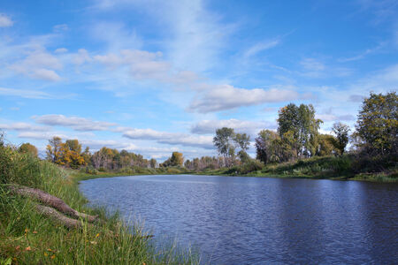 Scenic autumn landscape calm river yellow-green trees on the shore and white clouds on blue skyの写真素材
