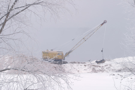 Winter landscape a yellow excavator on the river bank in thick fog produced sandの写真素材