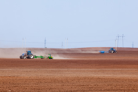 spring landscape tractor plowing endless field against the blue sky and the power line on the horizon の写真素材