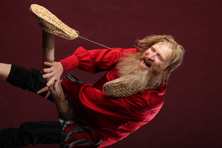 portrait of a man in a red shirt with long hair beard and mustache with a baton and bast shoes in...