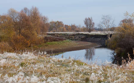 Scenic autumn landscape  oak grove with yellowed leaves near the river, frost on the grass on a cold morningの写真素材