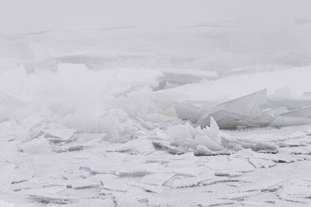 Winter landscape of dense fog on the river ice and trees covered with frost on the shoreの写真素材