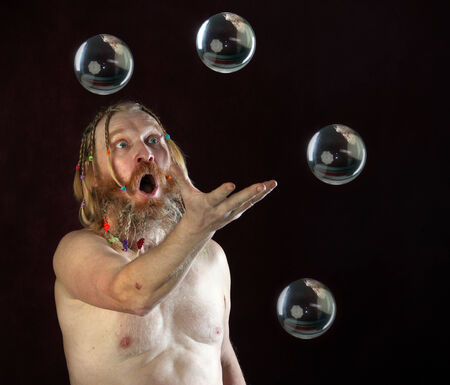 close-up portrait of a man with a long beard, mustache and hair braided in pigtails plays with glass sphere studio on dark backgroundの写真素材