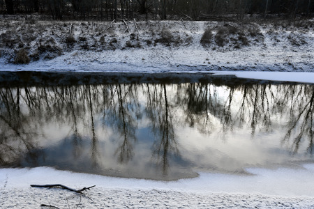 beautiful winter landscape reflection of trees in water quiet river on a cloudy dayの写真素材