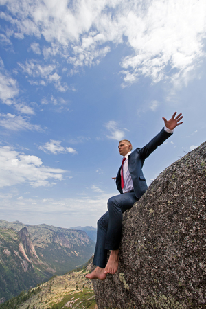 portrait of a young man in a business suit at the top of the mountain on the background of mountains and blue sky on a sunny summer dayの写真素材