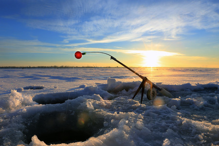 close-up drill, fishing rod near the hole on the ice in winter river at sunsetの写真素材