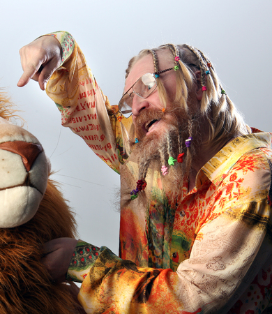 close-up portrait of an adult male with African braids beard and mustache in a colorful shirt playing with toy lion studio for light gray backgroundの写真素材