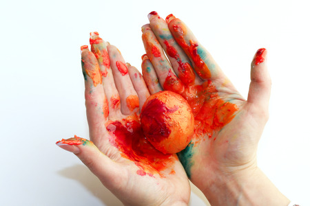 close-up of a single egg in the orange paint in female hands on a light background studioの写真素材