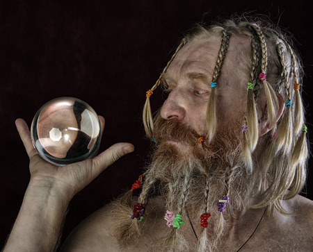 close-up portrait of a man with a long beard, mustache and hair braided in pigtails plays with glass sphere studio on dark backgroundの写真素材
