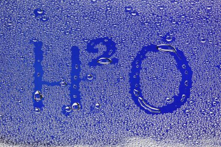 close-up texture of water drops on glass with the inscription formula H2O on a blue backgroundの写真素材