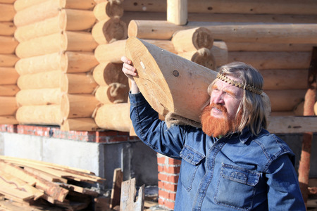 close-up portrait of man with a log in his hand against the background of the new log house on a sunny dayの写真素材