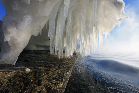 Macro bizarre of snow, ice and icicles on the rocky banks of the river in the sunshine, low angle...