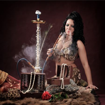 portrait of oriental girls on burgundy background in the studio smoke hookah and dance