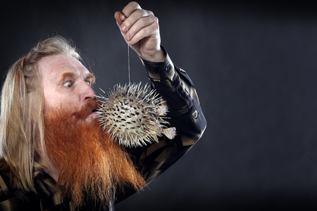 Portrait of an adult man with a red beard and mustache with the globefish on a dark background...