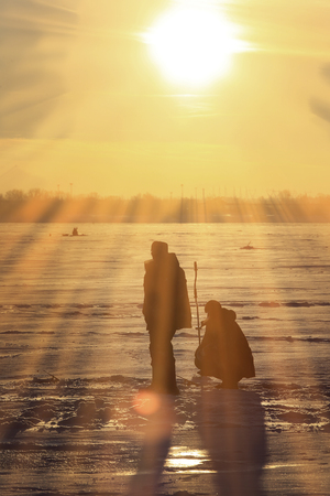 winter landscape fishermen on the ice of the river at sunsetの写真素材